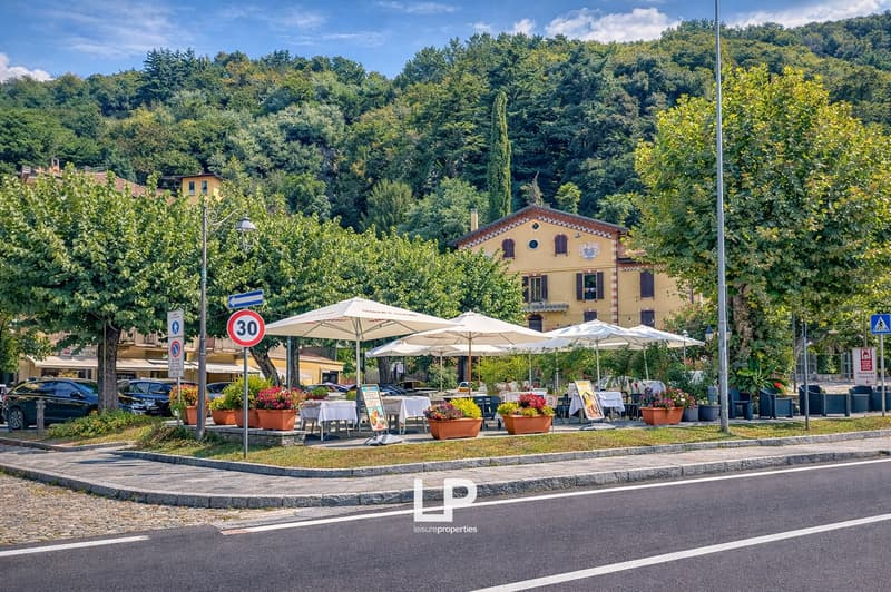 Outdoor dining area, flower pots, cars parked on the side, yellow building, speed limit sign, green trees and bushes