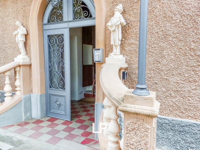 Facade of a building, entrance with wooden and metal door, tiled entrance floor, decorative statues, wall with textured finish