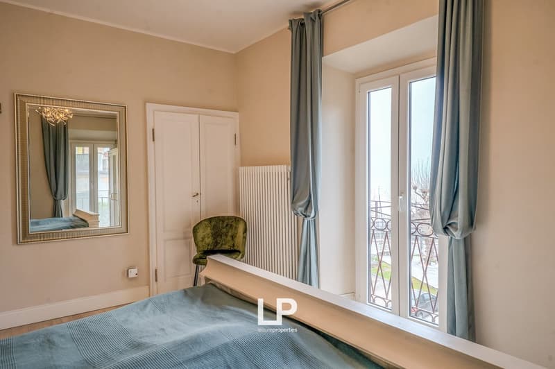 Bedroom with bed, chair, mirror, radiator, large windows with view outside