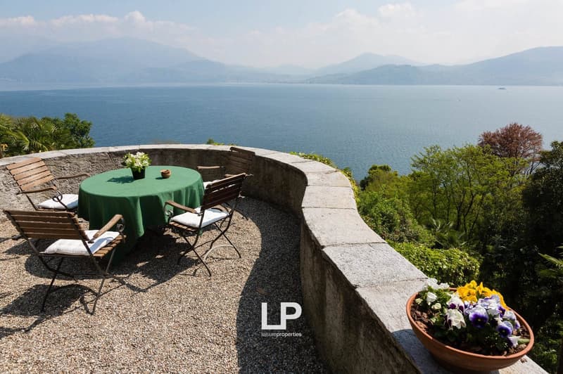 stone wall, green table, wooden chairs, flowers, gravel surface, sea view