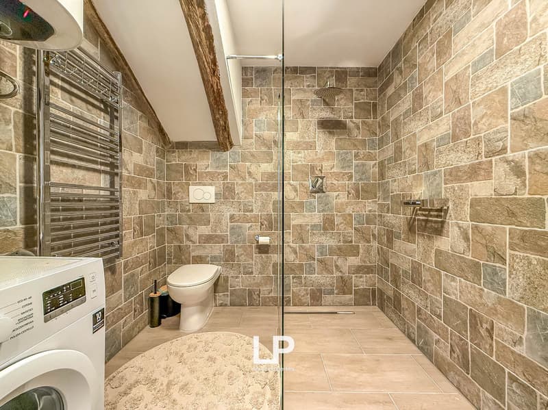 bathroom with shower, tile wall, toilet, washing machine, towel radiator