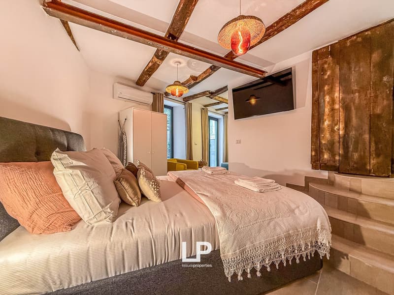 A bedroom with large bed, blankets, pillows, a cabinet, TV, mirrors, and wooden beams on the ceiling.