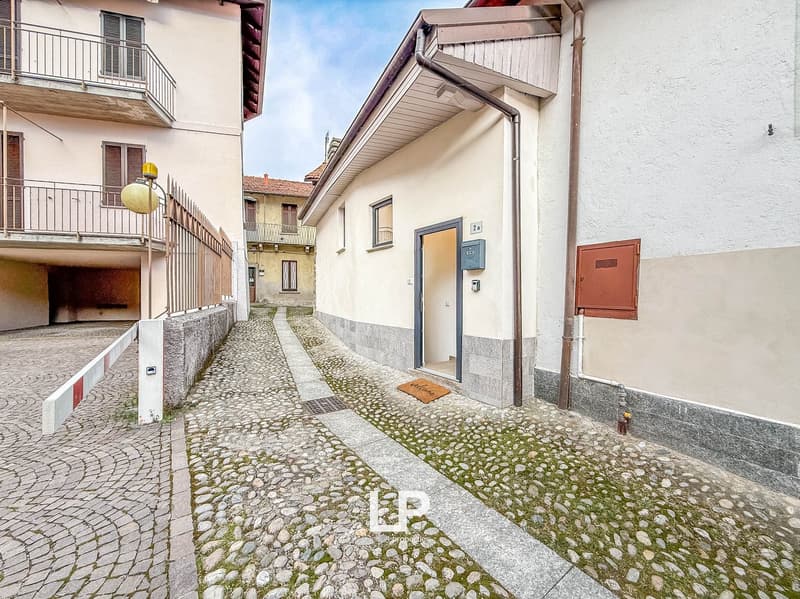 Building exterior with cobblestone street, balcony on first floor, closed entrance door, and side alley with fence.