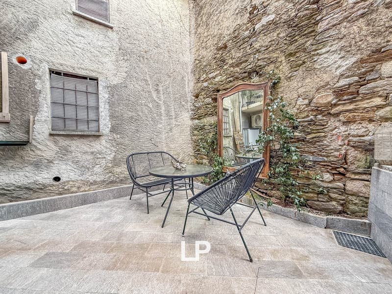 Small courtyard with tiled floor, chairs, table, mirror, and climbing plants on stone wall