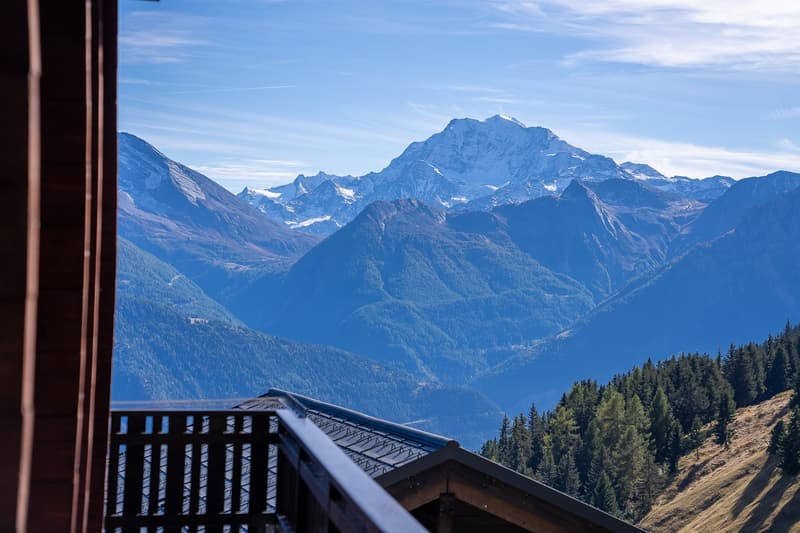 View from balcony: mountains and hills in the distance, clear sky with scattered clouds, a wooden balcony with black railings