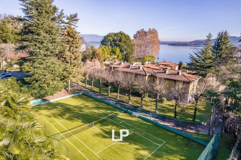 Tennis court in a green area with trees, a house with red roof and windows