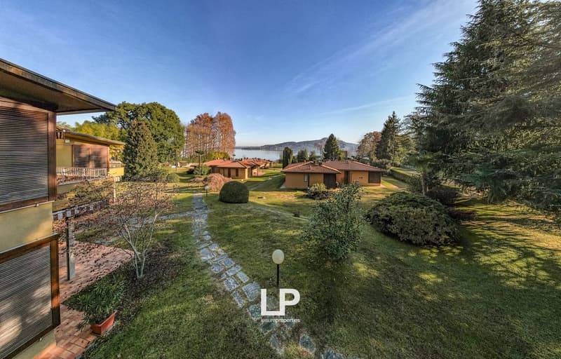 Multiple villas, paved path, green lawn, bush, potted plant, trees, mountain range, lake