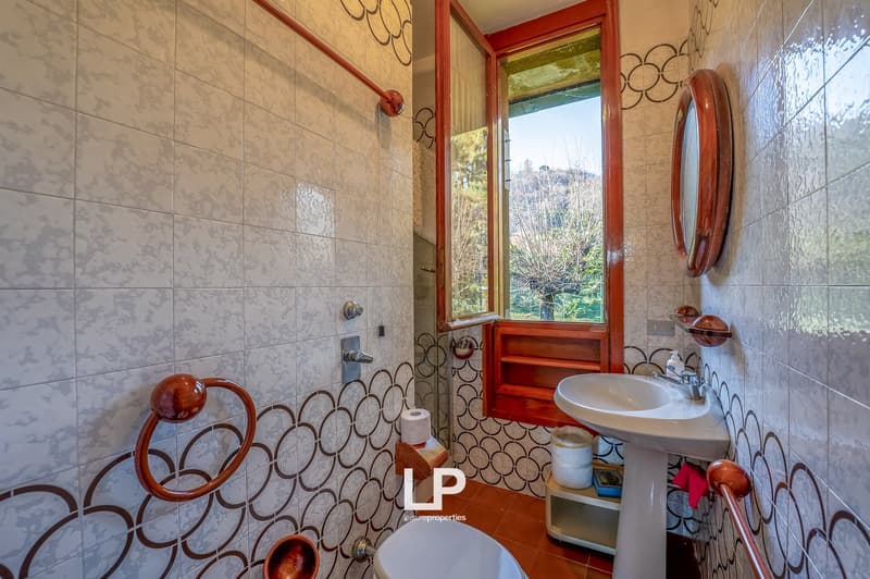 Bathroom with white ceramic tiles, wooden window frame, a sink with faucet, and a toilet.