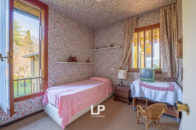 single bed, nightstand, lamp, TV on table, shelves, window, curtains, floral wallpaper, balcony with railing