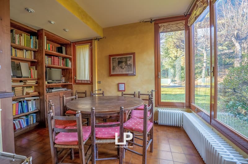 large table, 6 chairs, wooden floor, radiators, bookshelves with books, picture frame on the wall, windows, greenery outside
