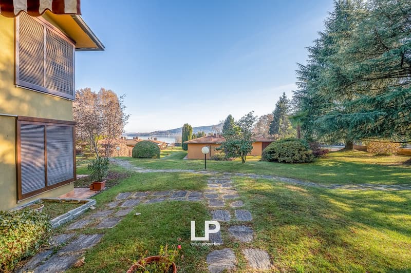 well-maintained garden, stone pathway, large trees, grassy lawn, shrubs, water view