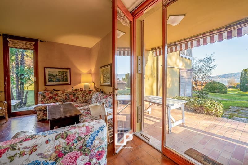 Living room: 2 couches, wooden coffee table, floor lamp, picture frames, glass door, glass windows, tiled floor, wooden bench, tiled outdoor space, greenery
