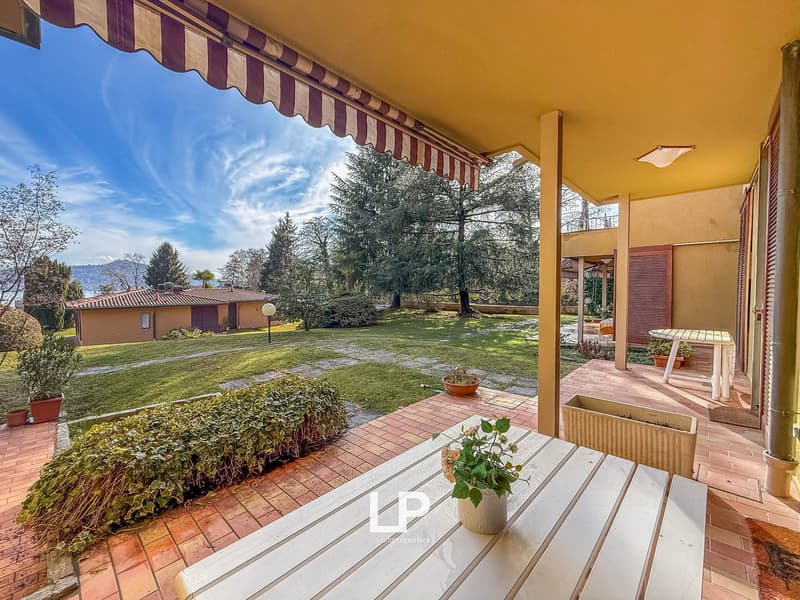 covered patio, brick flooring, table, chairs, plants, distant house, trees, grass, mountain