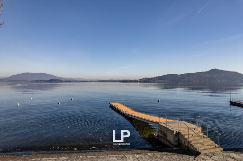 Beautiful landscape view of lake and mountains, concrete walkway leading to lake, buoys in the water, calm water, blue sky.