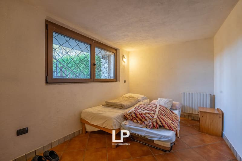 2 beds, white linen, white walls, brown tiled floor, heater on wall, small window, power outlet on wall, shoes on floor