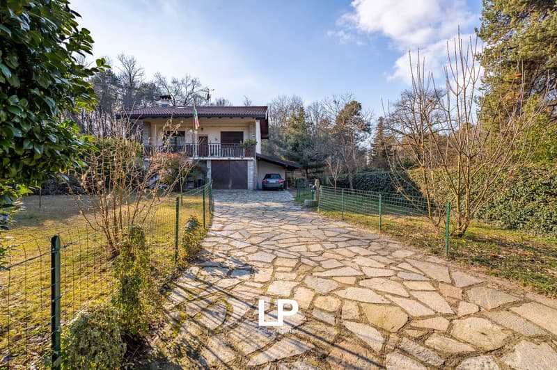 Detached house, paved driveway, green lawn, garage, balcony, surrounded by trees