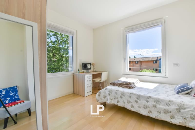 Bedroom with bed, desk, chair, monitor, windows with view of the outside.