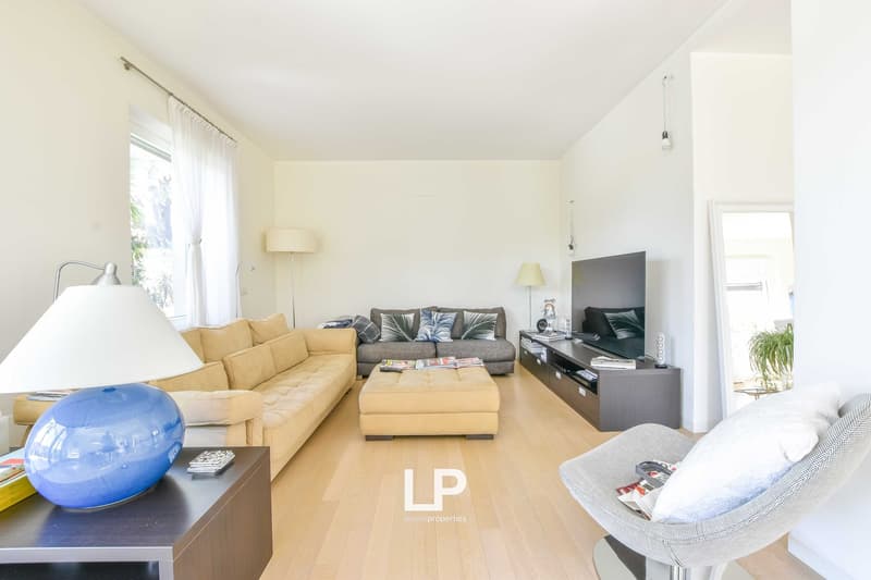 Spacious living room with large windows, hardwood floors, yellow sofa, gray couch, TV stand, and a blue inflatable chair