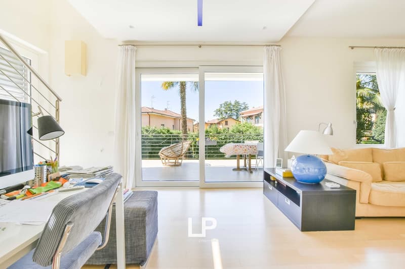 Spacious living room with large windows overlooking a balcony, comfortable sofa, coffee table, and various decor elements.