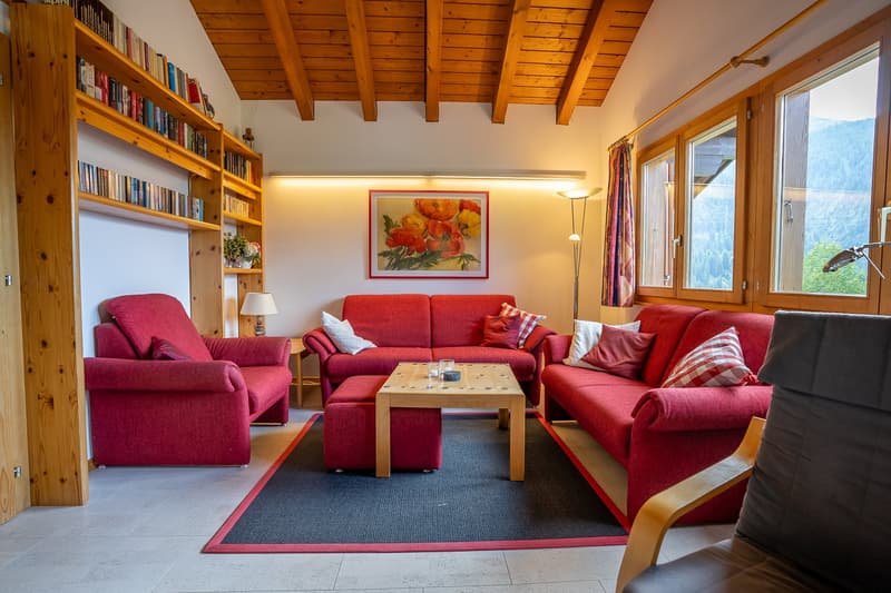 living room with red couches, wooden table, wooden ottoman, bookshelves, lamps, picture frame, carpet, view of mountains