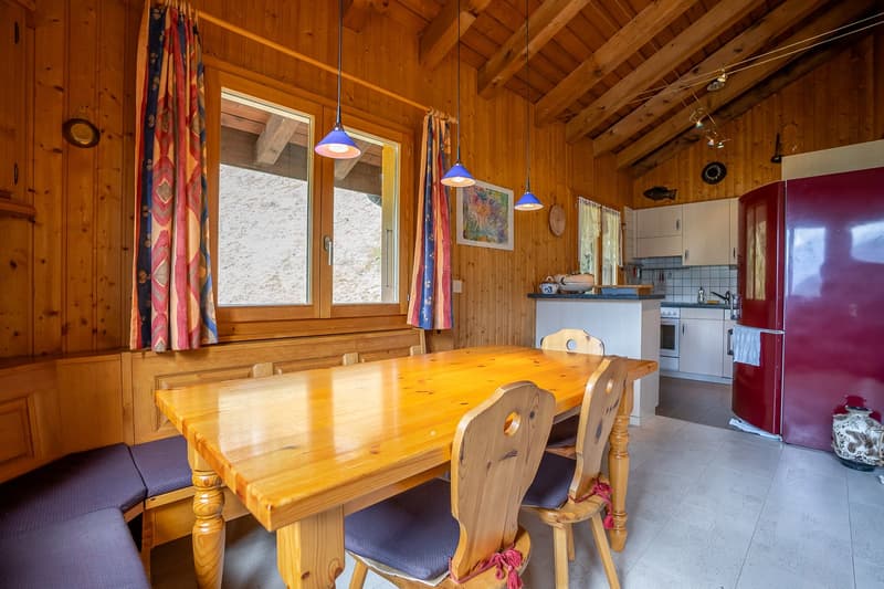 Dining room with a large wooden table and four chairs, wooden walls, a kitchen area with a counter and a refrigerator