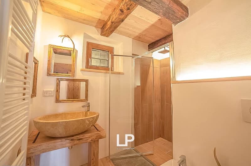 Stone sink, large mirror, wooden window frames, wooden beams on the ceiling, tiled shower