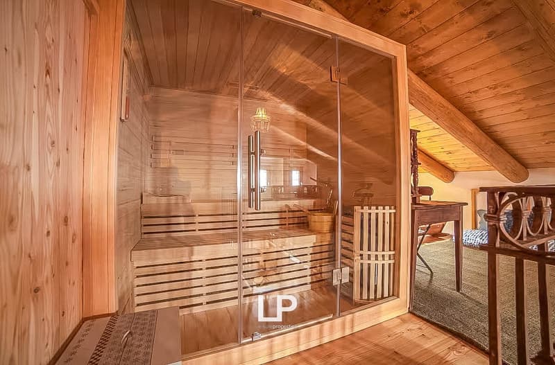 A wooden sauna with a wooden bench and glass walls, a lamp mounted on the wall