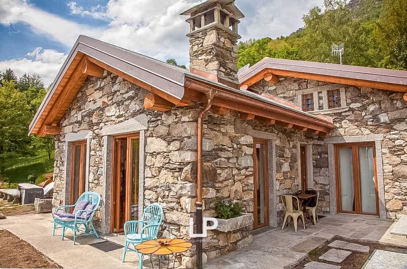 stone walls, brown roof, fireplace, view of hills, table and chairs on porch