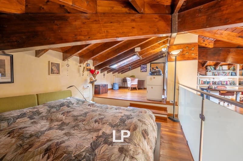 wooden exposed beams, wooden flooring, bed with headboard, green headboards, balcony, wardrobe, shelves with books, desk, office chair, lamp, paintings on wall, chest, radiator, picture frame, window