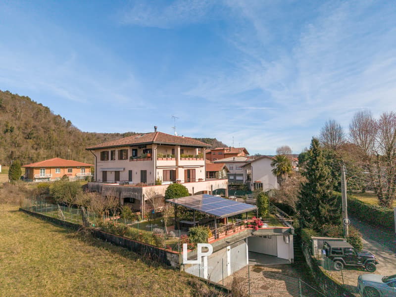 large villa, red roof, white exterior walls, balcony, attached garage, garden with trees and shrubs, fenced yard