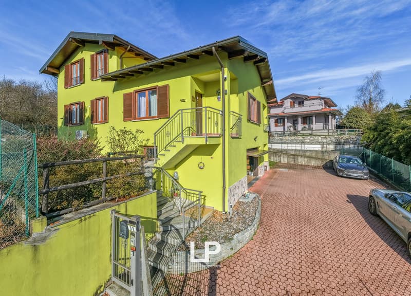 2 story house, bright yellow paint, metal handrails, outdoor staircase, 2 cars parked, fenced perimeter, brick driveway