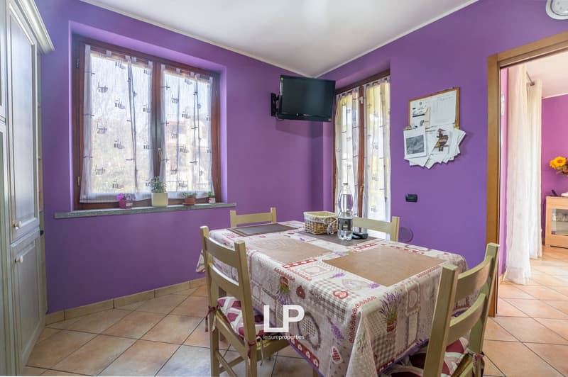 Dining room with table and chairs, purple walls, windows, television, flower vases, tiled floor