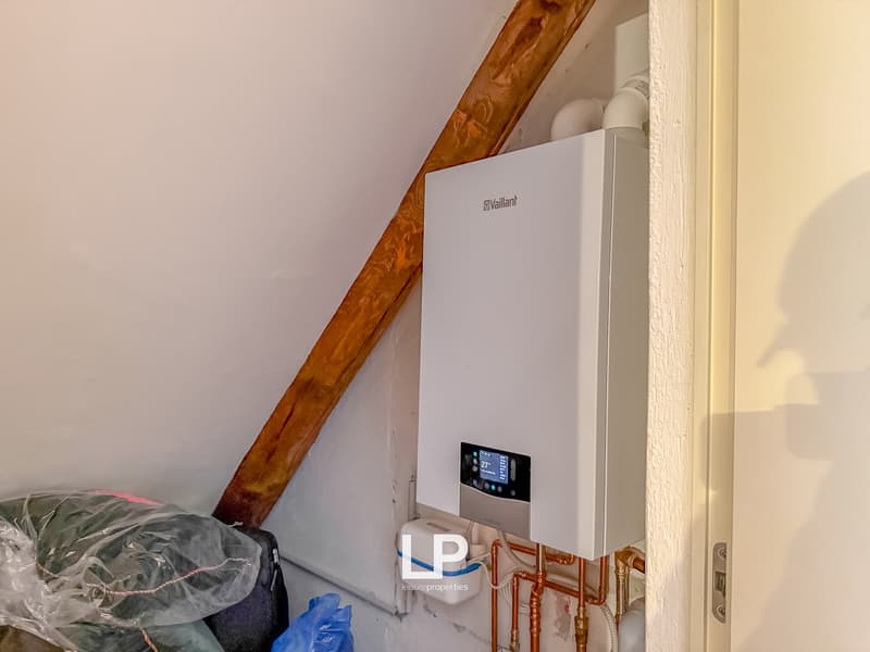 White water heater against a white wall, copper piping, a wooden beam