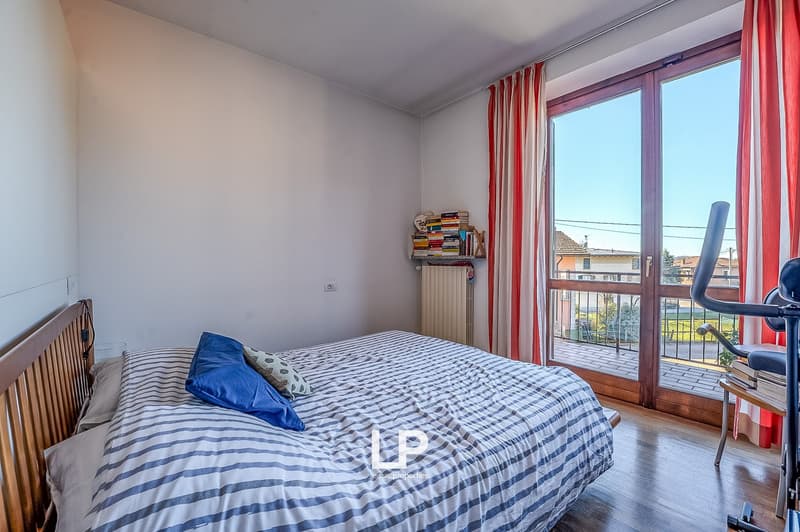 double bed, blue pillows, white and blue striped bedsheets, wooden nightstand, exercise machine, glass door to balcony, radiator