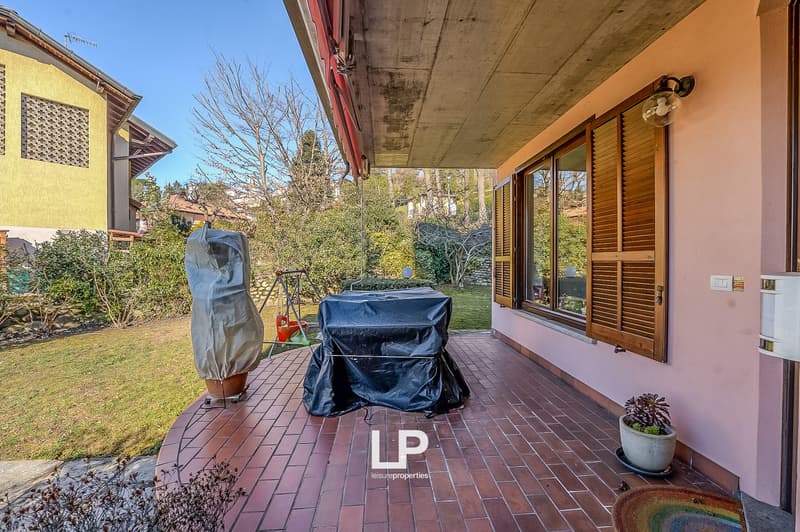 Terrace with brick flooring, wooden doors, covered area, table covered with black cloth, and outdoor plant in a pot.