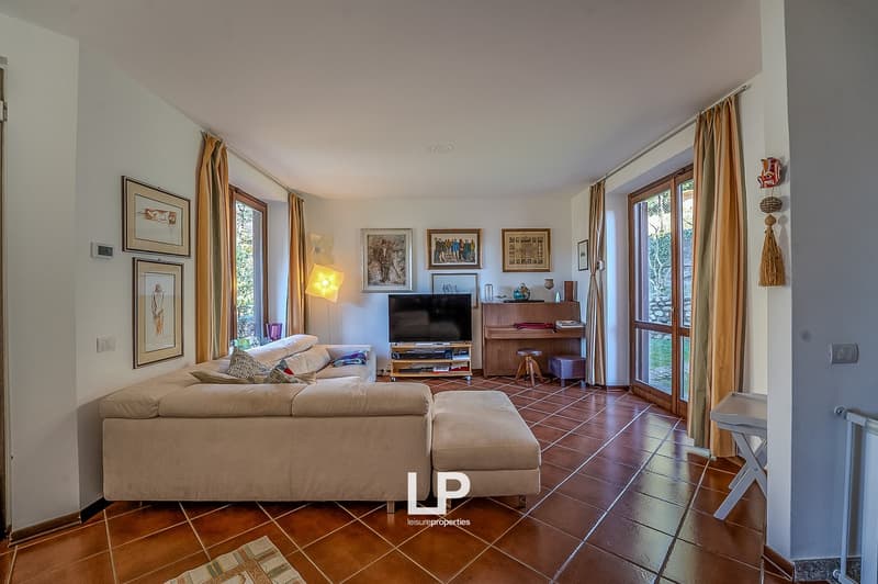 modern living room, beige sofa, ottoman, floor-mounted flat screen TV, wooden piano, wooden bar stool, lamps, tiled floor, open window