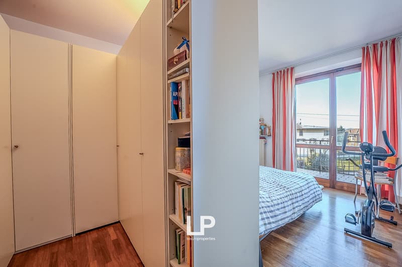 a bedroom with wooden floor, bed, bedside table, large closets, and window with terrace access