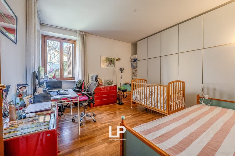 Bedroom with two single beds, crib, study table with computer, red wardrobe, bookshelves, picture frames