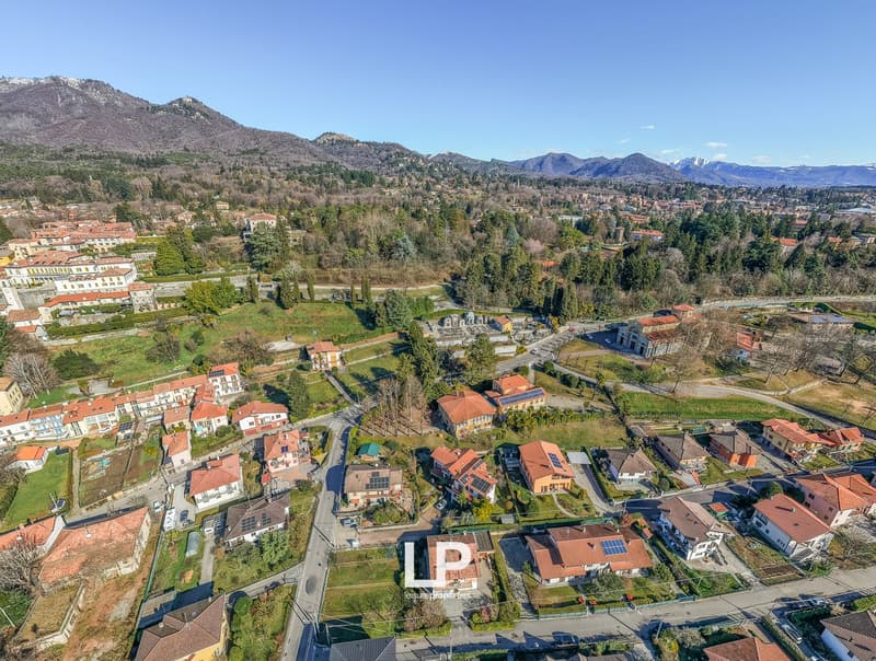 Aerial view of a village with several houses, solar panels, mountains, greenery, and winding roads.