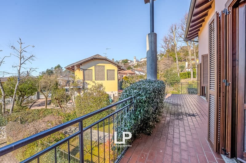 House with a balcony, brick tiled floor, metal railing, a large bush and yellow painted house