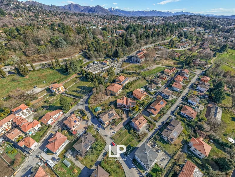 Residential neighborhood with houses, trees, solar panels, roads, clear sky, and mountains in the background.