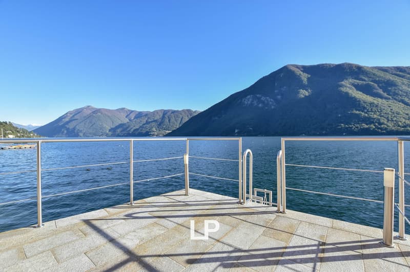 Terrace with stone flooring, stainless steel railings, clear blue lake, mountains in the background