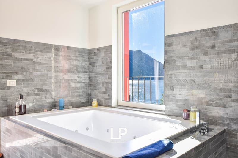 jacuzzi, white tiled wall, blue towel, toiletries on counter, glass window, balcony with mountain view
