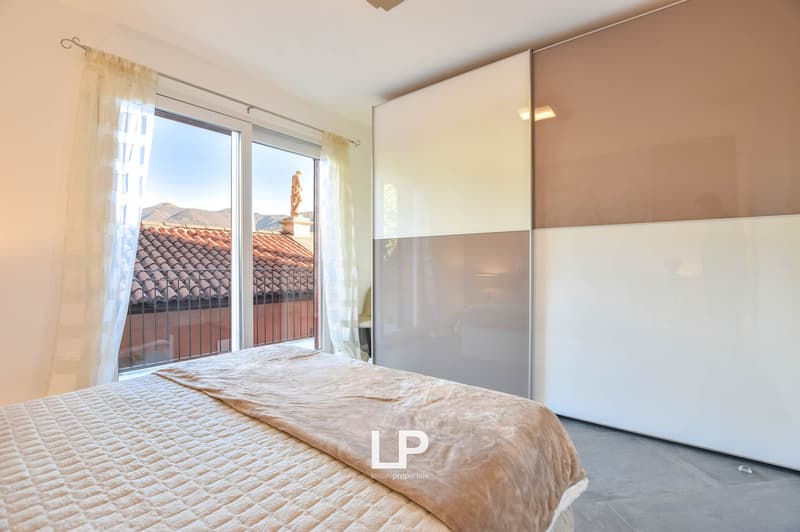 Spacious bedroom with a double bed, windows with views of the mountains, minimalist wardrobe, tiled flooring, and a balcony.
