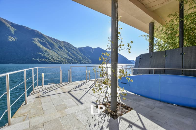 Balcony with stone floor, railings, plant, and view of water and mountains.