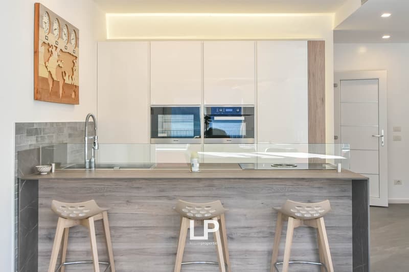 modern kitchen, wooden countertops, glass backsplash, white cabinetry, stainless steel appliances, large sink with faucet, three stools