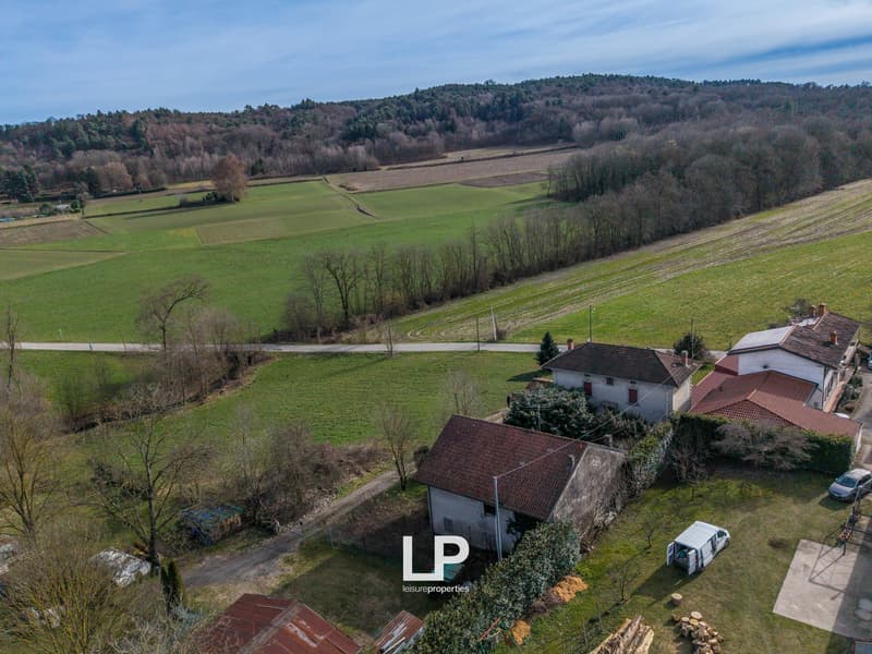 Aerial view of a rural property with several buildings, green fields, and a road in the distance.