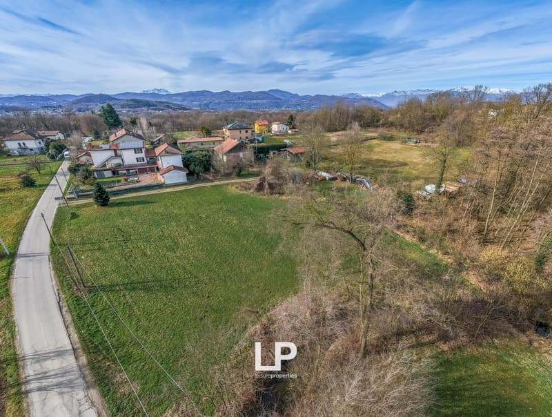 Aerial view of a rural area with several houses, green fields, and mountains in the background.