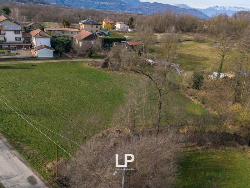 large open field, several houses in the background, mountains in the distance