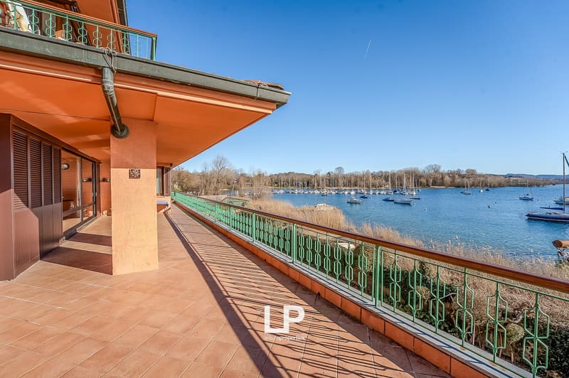 Balcony with green railings, tiled floor, view of a lake with boats